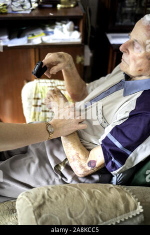 Ein Bezirk Krankenschwester behandelt einen 90 vier Jahre alten Mann, der Gehirn- und Kopfverletzungen nach einem traumatischen Fallen zu Hause, nach seiner Entlassung aus dem Krankenhaus. Stockfoto