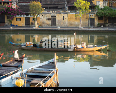 Hölzerne Fischerboote mit Augen auf Rümpfe in den Thu Bon Fluss in Hoi An, Vietnam angedockt gemalt. Gold Stuck Gebäude Leben am Fluss. Stockfoto