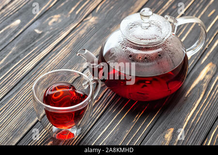 Red Hibiscus Tee im Glas Teekanne und Tasse auf hölzernen Tisch Stockfoto