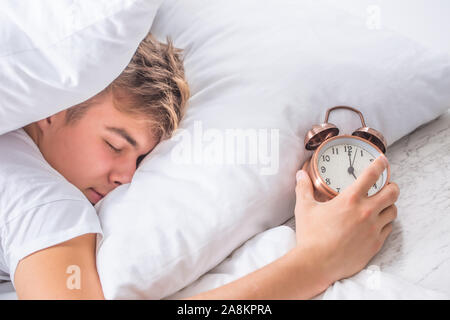 Junger Mann mit Wecker schlafen auf dem Bett. Stockfoto