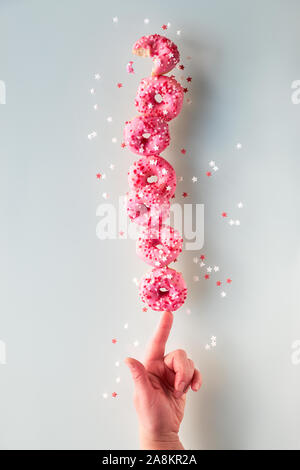 Kreative Bild der vollkommenen Balance, Turm oder Pyramide von leckeren Rosa donuts Balancieren auf Zeigefinger der weiblichen Hand. Konzeptionelle Gleichgewicht auf Neutral Stockfoto