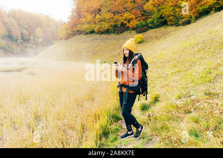 Hipster girl Wanderer auf einem Forstweg sieht am Telefon Gadget und lächelt. Stockfoto