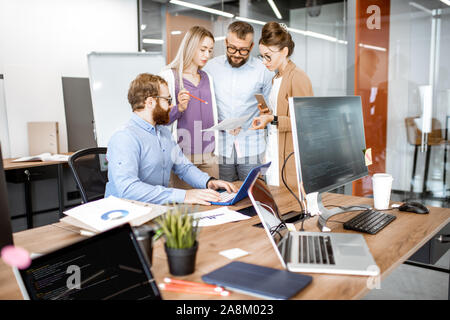 Gruppe von verschiedenen Kolleginnen und Kollegen arbeiten in modernen Büros, Diskussion oder kleine Konferenz auf einem Arbeitsplatz mit Computer Stockfoto