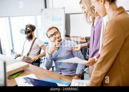 Gruppe von verschiedenen Kolleginnen und Kollegen, die im Büro, in der Diskussion oder eine kleine Konferenz am Arbeitsplatz Stockfoto