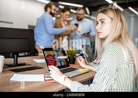 Porträt einer jungen Frau, die als Web Designer im Büro mit Kollegen auf dem Hintergrund Stockfoto