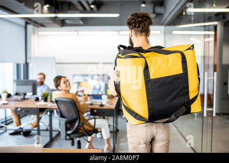 Kurier liefern Produkte für Büro, tragen gelbe Thermal bag, Ansicht von der Rückseite. Konzept der Lebensmittel Auslieferung an die Mitarbeiter im Büro Stockfoto