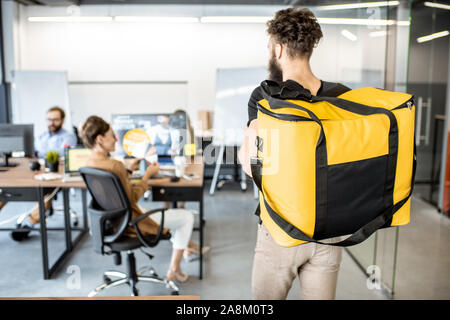 Kurier liefern Produkte für Büro, tragen gelbe Thermal bag, Ansicht von der Rückseite. Konzept der Lebensmittel Auslieferung an die Mitarbeiter im Büro Stockfoto