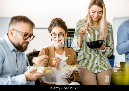 Gruppe von verschiedenen Kollegen essen Takeaway Salat, zusammen zu sitzen und Spaß haben während einer Mittagspause im Büro Stockfoto