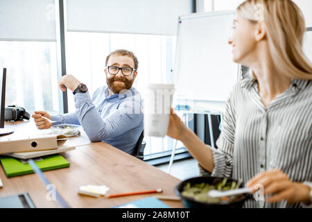 Mann und Frau Salat und Kaffee trinken während einer Mittagspause am Arbeitsplatz ohne das Büro zu verlassen Stockfoto