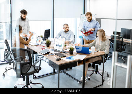 Gruppe von verschiedenen Kolleginnen und Kollegen arbeiten in modernen Büros, Diskussion oder kleine Konferenz auf einem Arbeitsplatz mit Computer Stockfoto