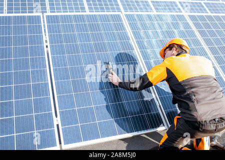 Gut ausgestattete Arbeiter in Schutzkleidung orange Kleidung Installation von Sonnenkollektoren, der Neigungswinkel messen auf eine Photovoltaik Anlage auf dem Dach Stockfoto