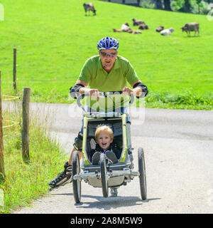 Mann eine skating Tour auf Inline Skates mit seinem kleinen Sohn im Buggy Stockfoto