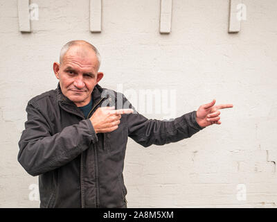 Der grauhaarige Mann zeigt die Richtung an, mit seinen Fingern. Ein Mann mit einer Glatze. Menschen. Stockfoto