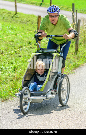 Mann eine skating Tour auf Inline Skates mit seinem kleinen Sohn im Buggy Stockfoto