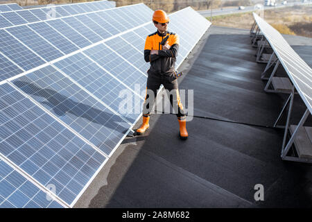 Porträt eines gut ausgestatteten Arbeiter in Schutzkleidung orange Kleidung Prüfung von Solarzellen auf dem Dach eine Photovoltaik Anlage. Konzept der Wartung und Installation von Solar- Stationen Stockfoto