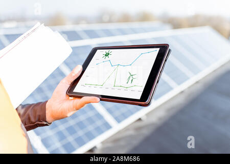 Mann mit digitalen Tablet auf einem solar Station, close-up auf einem Tablet Bildschirm mit einem Diagramm von Solar- und Windenergie täglich Generation. Konzept der on-line-Überwachung der E-Station Stockfoto