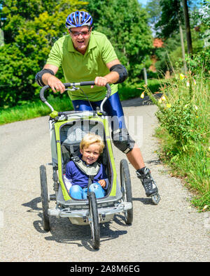 Mann eine skating Tour auf Inline Skates mit seinem kleinen Sohn im Buggy Stockfoto