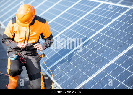 Gut ausgestattete Elektriker Connecting Solar Panels, die Spannung prüfen und anschließen Verkabelung auf einer Photovoltaikanlage auf dem Dach Stockfoto