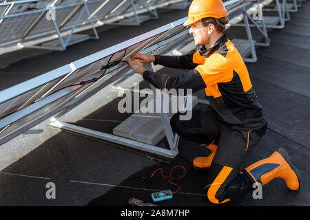 Gut ausgestattete Elektriker Anschließen der Drähte von Solarzellen auf einem Dach Photovoltaikanlage. Konzept für die Installation von solar-Stationen Stockfoto