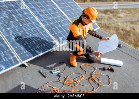 Elektriker in arbeitsschutzausrüstungen Installation von Solarzellen auf einem Dach mit Blueprints und Werkzeuge Stockfoto