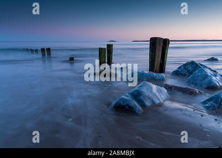 Ausgehende Wellen und Flut. Treffen rund um die buhnen und Felsen. Die blaue Stunde auf Youghal Strand. Stockfoto