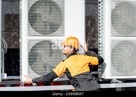 Professionelle Arbeiter in Schutzkleidung Installation der Außeneinheit der Klimaanlage oder Wärmepumpe auf dem Dach Stockfoto