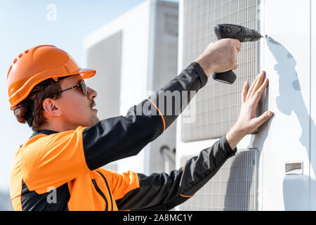 Professionelle Arbeiter in Schutzkleidung installieren oder reparieren Außeneinheit der Klimaanlage oder Wärmepumpe auf dem Dach Stockfoto