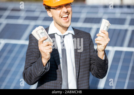 Portrait einer aufgeregt Geschäftsmann mit Geld von der Stromerzeugung eines solar Station erworben. Konzept für erfolgreiche Investitionen in alternative Energie Stockfoto