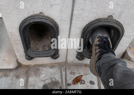 Mann sauber seine Schuhe auf der boot Abstreifer in eine niedrige Mauer am Eingang zum Antrieb eines Reihenhauses. Metall Bogen mit Gesicht nach oben geprägt. Kleinen Hohlraum für Stockfoto