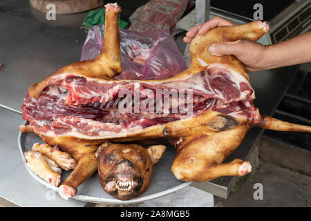 Ein Hund wird angezeigt in Stücke zum Verkauf als Lebensmittel für den menschlichen Verzehr in einer Metzgerei in Vietnam. Weite Einstellung mit Metzger hand Stockfoto