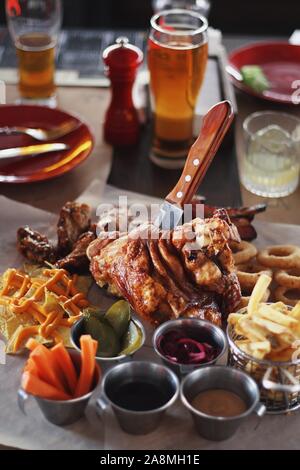 Schweinshaxe mit Karotte, Gurke, Soße und leichte filtrierte Bier in der Kneipe Tabelle Hintergrund. Leckere Drinks und Essen. Oktoberfest Traditionen, delici Stockfoto