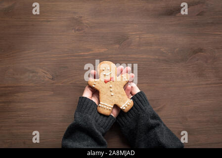Gingerbread Man in Hände auf Holz- Hintergrund. Weihnachten gemütliche Komposition - Hände halten hausgemachte Gingerbread Man cookie, Ansicht von oben, kopieren. Stockfoto
