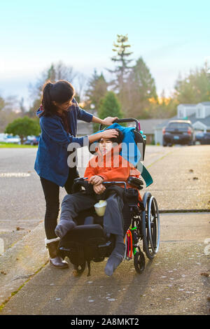 Big jugendlich Schwester trösten traurig deaktiviert kleiner Bruder im Rollstuhl beim Gehen im Freien Stockfoto