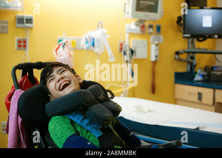 Deaktiviert 13 Jahre alt jugendlich Junge im Rollstuhl lächelnd neben seinem Krankenbett Stockfoto