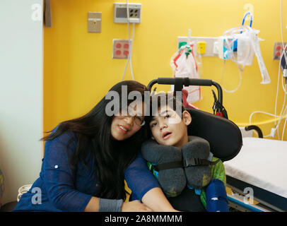 Lächelnd sitzen Mutter neben behinderten Sohn im Rollstuhl bis zum Krankenbett, zusammen gesprochen Stockfoto