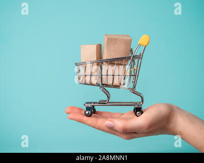 Spielzeug Warenkorb mit Boxen in weiblicher Hand über blauen Hintergrund. Kopieren Sie Platz für Text oder Design. Ssale, Rabatt, shopaholism Konzept. Konsumgesellschaft Trend Stockfoto