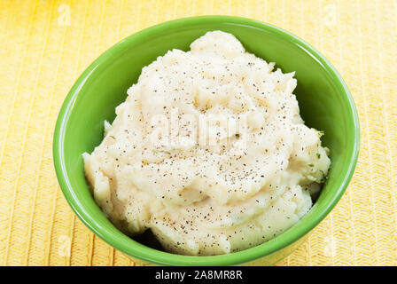 Blick von oben auf eine Schüssel mit hausgemachtem Kartoffelpüree in einem hellgrünen Schüssel. Die warme und frische Schlagsahne Kartoffeln werden mit schwarzem Pfeffer und zerlassener Butter gekrönt Stockfoto