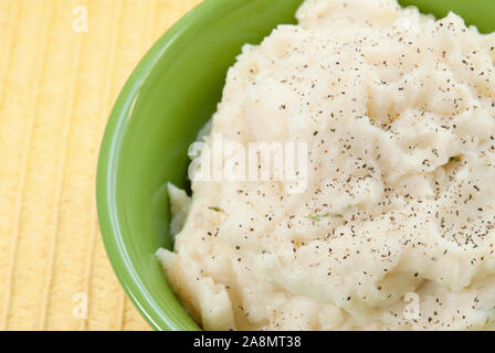 Einen hellgrünen Schüssel voll mit hausgemachtem Kartoffelpüree. Die warme und frische Schlagsahne Kartoffeln werden mit schwarzem Pfeffer und zerlassener Butter gekrönt. Stockfoto