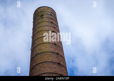 Ein großer Ziegelstein Schornstein bis zu einem blauen Himmel mit weißen Wolken. Verstorbenen industriellen gemauerten Schornstein gegen strahlend blauen Himmel Stockfoto