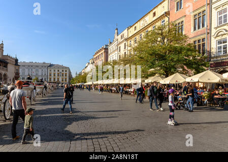 Menschen sitzen unter Sonnenschirmen auf Terrassen am Hauptplatz der Altstadt in Krakau, Polen an einem sonnigen Herbsttag Stockfoto