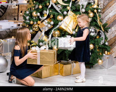 Porträt von zwei Schwestern tragen blaue Kleider neben geschmückten Weihnachtsbaum Holding verpackte Geschenkboxen Teilen präsentiert auf Boxing Day Stockfoto