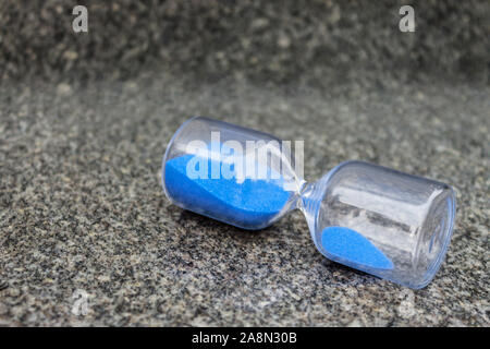 Glas Sanduhr mit blauem Granulat liegen auf grauem Granit Stockfoto