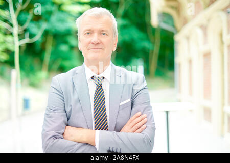 Portraitfotos von eleganten älterer Mann mit Anzug und Krawatte und stehen mit den Armen im Kreuz. Stockfoto