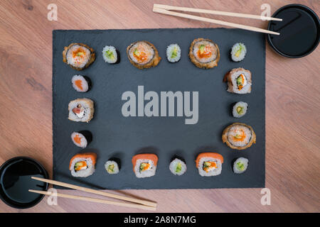 Schwarzer Schiefer mit Sushi mit Schüsseln mit Sojasauce und Stäbchen für Sushi, Ansicht von oben Stockfoto