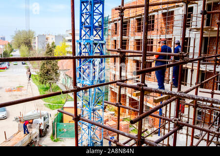 Rigger stehen auf Gerüst mit hölzernen Plattform hoch oben auf dem Gerüst über Baustelle. Stockfoto