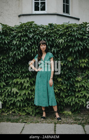 Frau mit einem eleganten grünen Kleid steht vor der Hedge Stockfoto