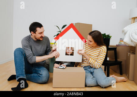 Junge durch ein Fenster eines Spielzeugs Papier Haus, von seinen Eltern gehalten Stockfoto