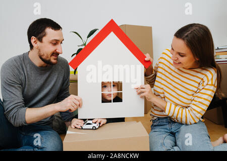 Junge durch ein Fenster eines Spielzeugs Papier Haus, von seinen Eltern gehalten Stockfoto