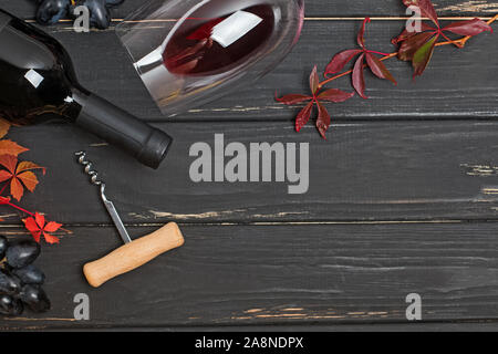 Flasche Rotwein, Wein Glas, Korkenzieher und Herbst rote Blätter auf schwarz Holztisch Stockfoto
