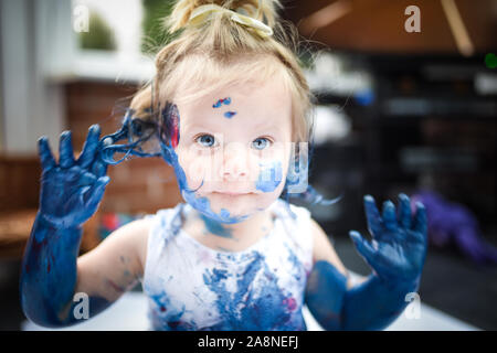 Eine entzückende kleine Kleinkind, Mädchen hat Spaß beim Spielen mit Farben malt, unordentlich und haben viel Spaß, in einer familiären Umgebung Schuß Stockfoto